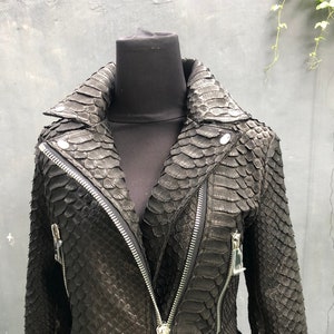 以下が含まれることがあります： ジッパー留めとベルトが付いた黒い革のジャケット。ジャケットはヘビ革製です。