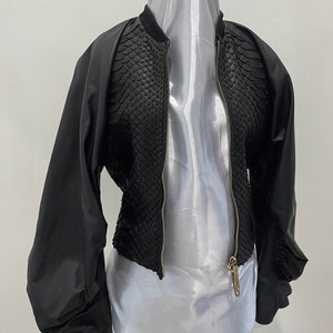 May include: A black bomber jacket with a snakeskin pattern on the front and solid black sleeves. The jacket has a zipper closure and a stand-up collar.