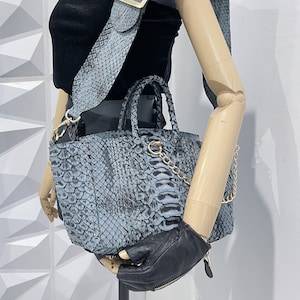 以下が含まれることがあります： ゴールドチェーンストラップと、それに合わせたヘビ柄のショルダーストラップが付いた、ブルーのスネークスキン製のトートバッグ。バッグはトップハンドルとジッパー開閉式です。