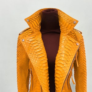 以下が含まれることがあります： ヘビ革製の黄色の革ジャン。ジッパー留めとスタンドカラーです。