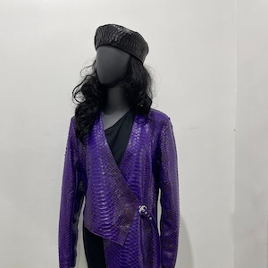 Peut inclure: Une veste en cuir de serpent violet avec une longue ligne d'ourlet asymétrique et un béret noir.