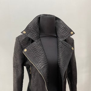 以下が含まれることがあります： ヘビ柄のブラックレザーのジャケット。ゴールドの金具が付いています。ジッパーで閉めることができ、襟があります。