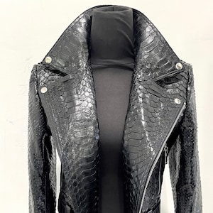 May include: A black leather jacket with a snakeskin pattern. The jacket features a wide collar, silver hardware, and a belt at the waist. The jacket is displayed on a black mannequin.