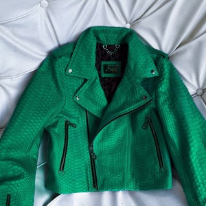 以下が含まれることがあります： ジッパー留めと黒のアクセントが付いた緑色のヘビ革のバイクジャケットです。