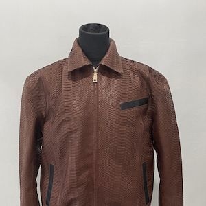 以下が含まれることがあります： ジッパー留めと黒のトリムが付いた、茶色のヘビ革のボンバージャケット。