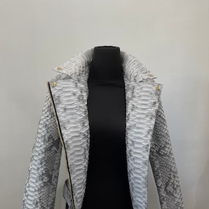 May include: A gray snakeskin leather jacket with a zipper closure and a belt. The jacket has a stand-up collar and long sleeves.
