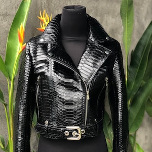 May include: A black leather jacket with a snakeskin pattern. The jacket features a zip fastening, a belt at the waist, and a stand-up collar.
