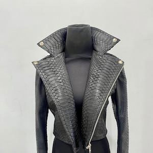 以下が含まれることがあります： 蛇柄の黒い革のジャケット。ジッパーで閉めることができます。襟が高く、袖が長いです。