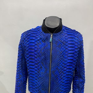 May include: A blue bomber jacket made of snakeskin. The jacket has a zipper closure and black ribbed cuffs and waistband.