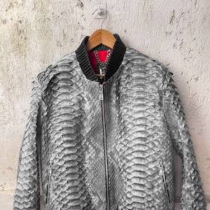 以下が含まれることがあります： 黒いジッパーと黒いリブ編みの袖口とウエストバンドが付いたグレーのヘビ革ボンバージャケットです。