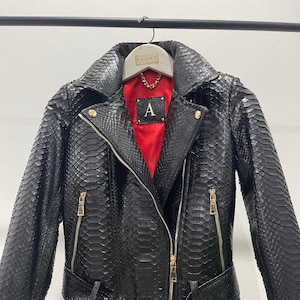 May include: Black leather jacket with a snakeskin pattern, gold zipper accents, and a gold belt with a buckle. The jacket has a red lining with a gold letter "A" on the inside.