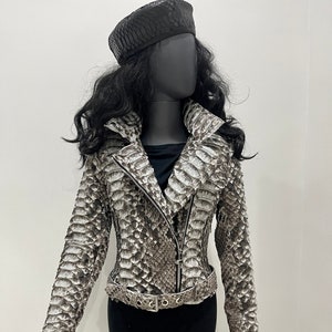 以下が含まれることがあります： ジッパー留めとベルトが付いた、茶色と白のヘビ革ジャケット。ジャケットはスタンドカラーと長袖です。