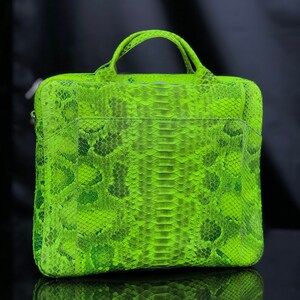 May include: A bright green snakeskin laptop bag with a top handle. The bag has a textured surface and a flap closure.