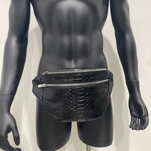 May include: A black leather fanny pack with a snakeskin pattern and two silver zips.