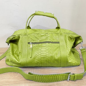 May include: A bright green duffel bag with a snakeskin texture. The bag features a top handle with silver studs, a zipped front pocket, and a detachable shoulder strap. The bag is made of a textured material and has a silver buckle.