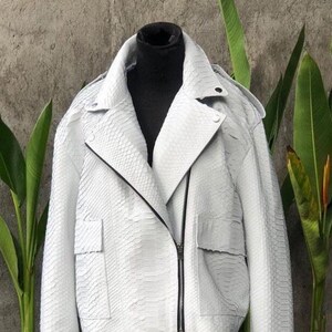 May include: A white leather jacket with a snakeskin pattern. The jacket has a zip fastening and two pockets.
