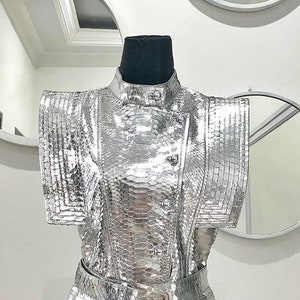 May include: A silver sequined top with a high collar and a belt. The top has a fitted silhouette and a slightly flared hem.