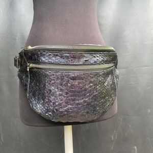 May include: A black snakeskin fanny pack with two zipped compartments. The bag is worn on a mannequin.