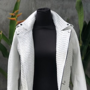 May include: White leather jacket with a snakeskin pattern. The jacket features a zip fastening, a belt, and a stand-up collar.