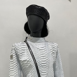 以下が含まれることがあります： 黒いジッパーと黒いベレー帽が付いた白いヘビ革ジャケット