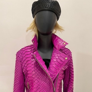 以下が含まれることがあります： 金色のジッパーが付いた明るいピンク色のヘビ革のジャケット。ジャケットはジッパー留めとスタンドカラーです。