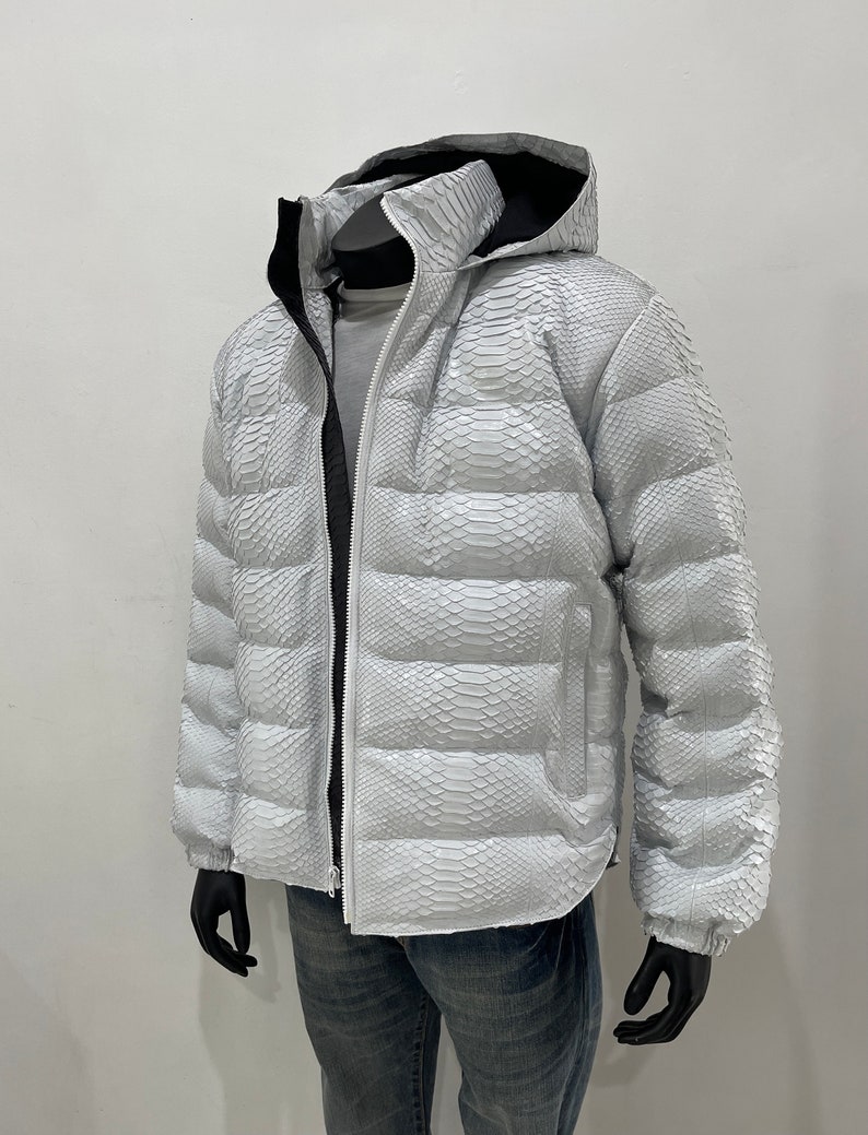 May include: A white puffer jacket with a snakeskin pattern. The jacket has a hood and a zip closure.