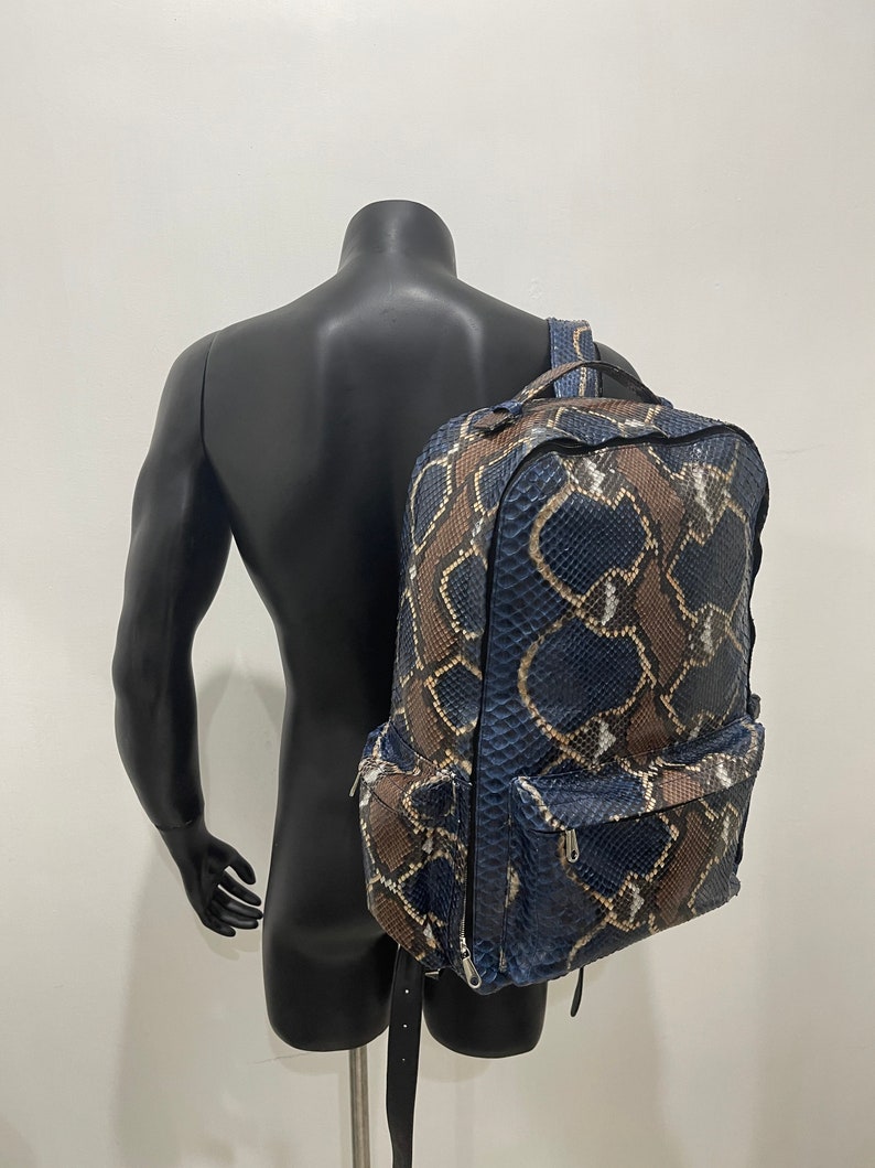 Op de afbeelding: Een blauwe en bruine slangleren rugzak met een ritsvak aan de voorkant.