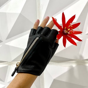 May include: Black leather fingerless gloves with a gold zipper detail. The gloves are worn by a person holding a red flower.