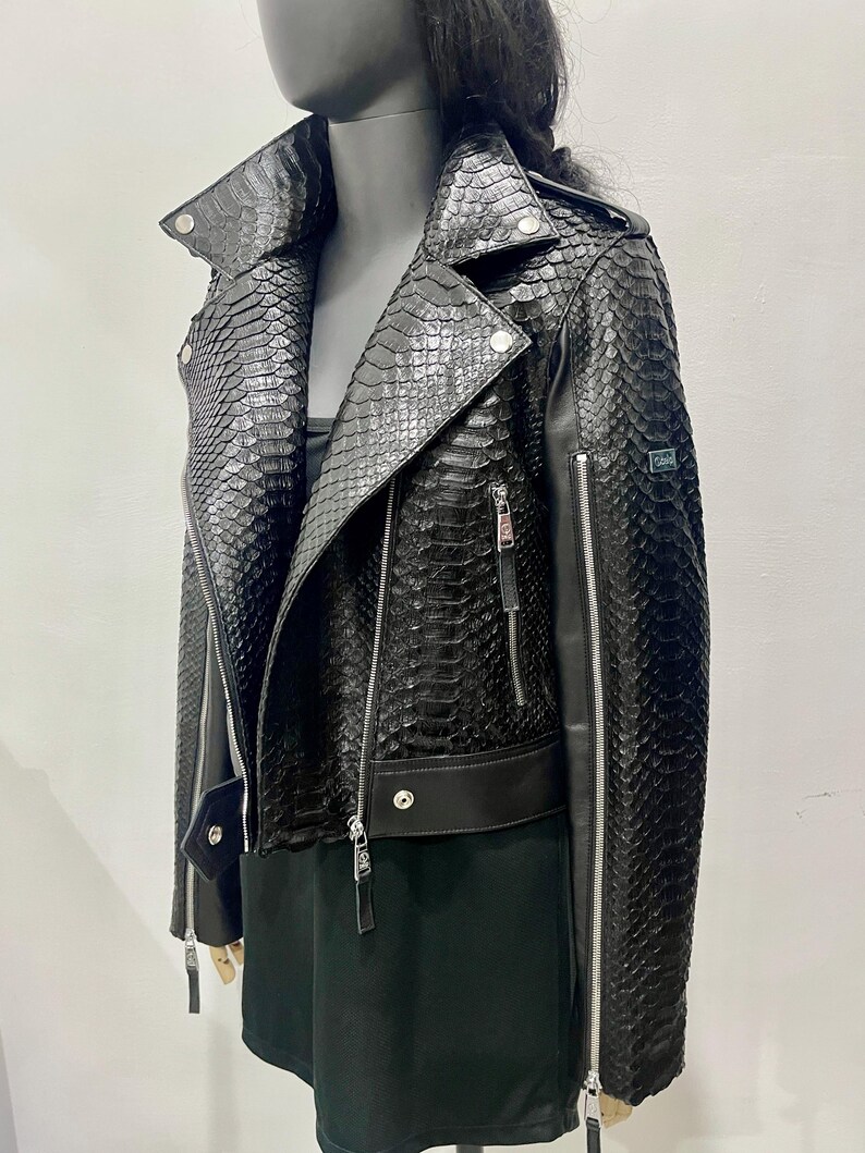 K&ouml;nnte beinhalten: Schwarze Lederjacke mit Schlangenhautmuster. Die Jacke hat einen Rei&szlig;verschluss und einen Stehkragen.