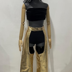 May include: Gold-coloured leather chaps with a snakeskin pattern and a black waistband. The chaps have a cutout design on the back of the legs.