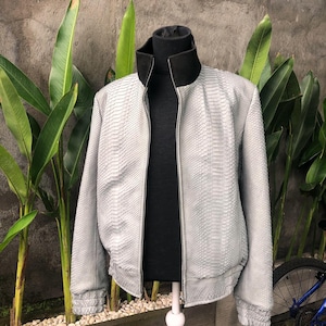 以下が含まれることがあります： 黒いジッパーと黒い襟が付いたライトグレーのヘビ革ボンバージャケット