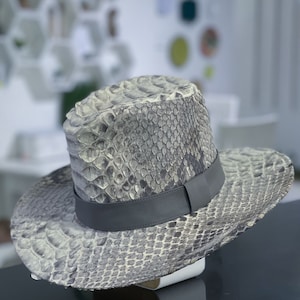 以下が含まれることがあります： グレーとホワイトのヘビ革のフェドーラハット。グレーの革のバンド付き