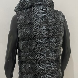 May include: A black sleeveless puffer vest with a snakeskin pattern. The vest has a hood and a zip closure.