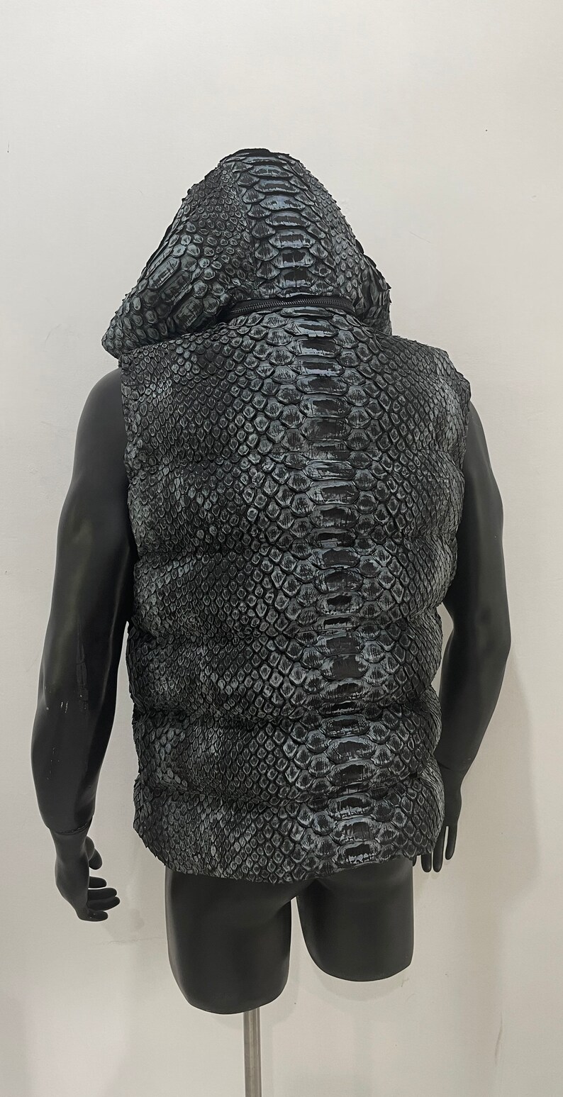 May include: A black sleeveless puffer vest with a snakeskin pattern. The vest has a hood and a zip closure.
