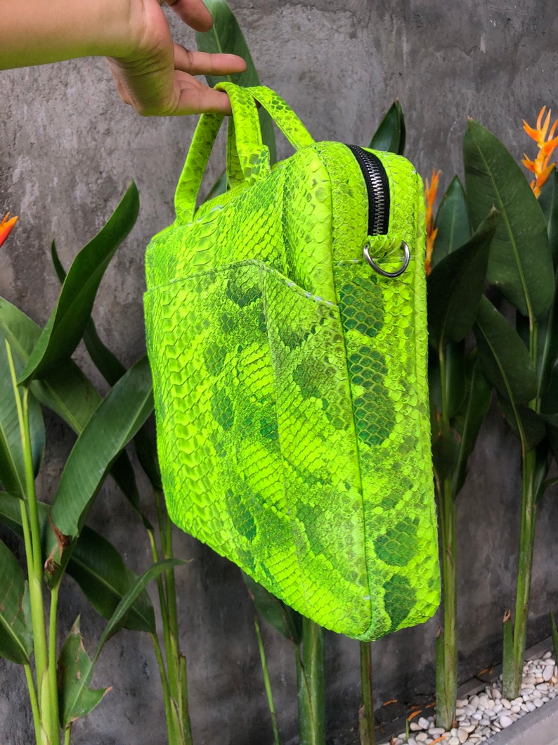 May include: A bright green snakeskin laptop bag with a zip closure and a silver ring handle.