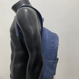 K&ouml;nnte beinhalten: Ein blauer Schlangenleder-Rucksack mit silberner Hardware. Der Rucksack wird von einer Schaufensterpuppe getragen.