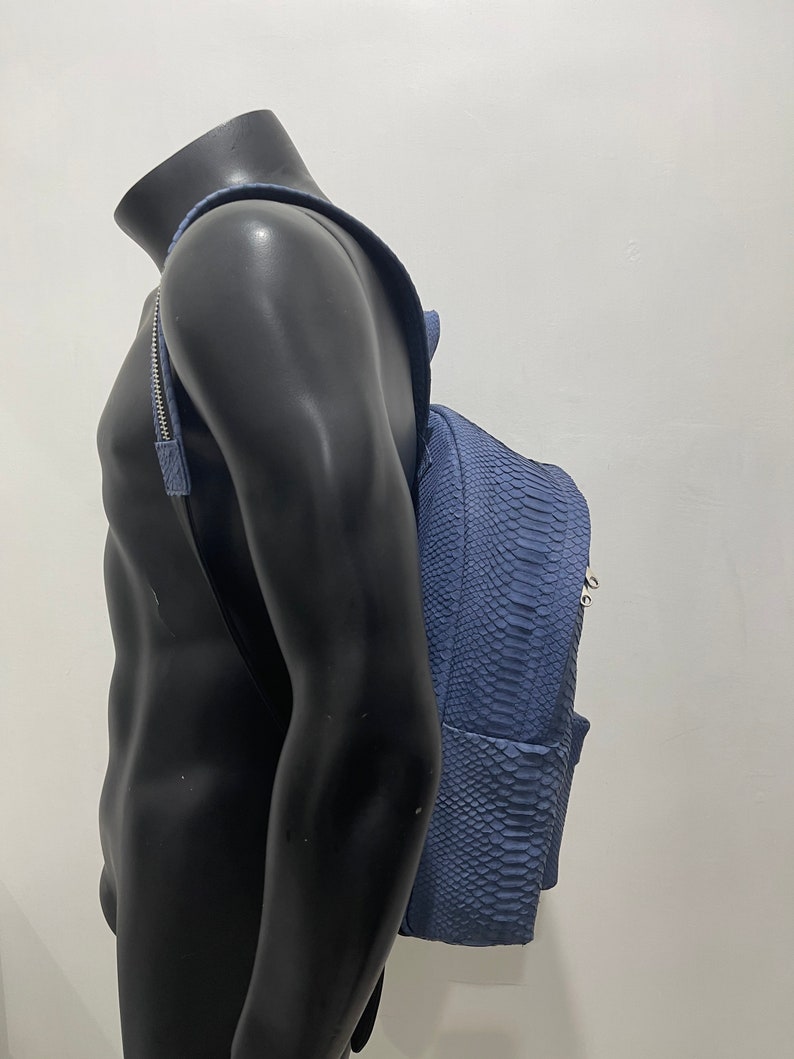 K&ouml;nnte beinhalten: Ein blauer Schlangenleder-Rucksack mit silberner Hardware. Der Rucksack wird von einer Schaufensterpuppe getragen.