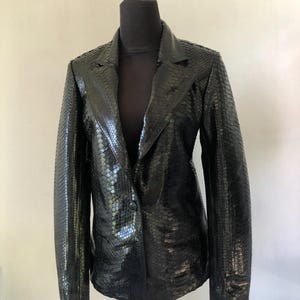 以下が含まれることがあります： シングルボタン留めの黒いヘビ革のブレザー。ブレザーはクラシックなフィット感で、滑らかで光沢のある仕上げです。