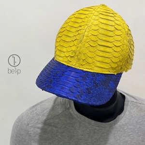 May include: A yellow and blue baseball cap made of snakeskin. The crown of the cap is yellow and the brim is blue.