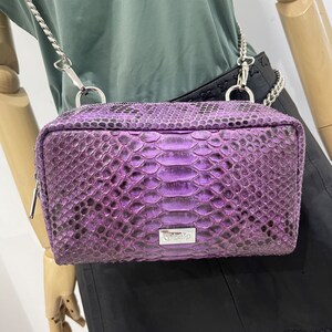 May include: A purple snakeskin crossbody bag with a silver chain strap and a silver logo that says "Obelp".