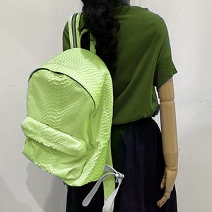 May include: A lime green snakeskin backpack with white straps. The backpack is being worn by a mannequin.