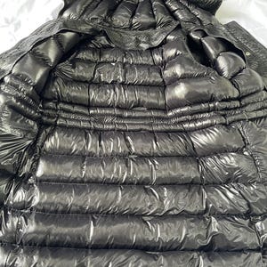 May include: A black, quilted puffer jacket with a hood. The jacket is made of a shiny, water-resistant material. The interior is also black and quilted. The jacket is designed for warmth and protection from the elements.