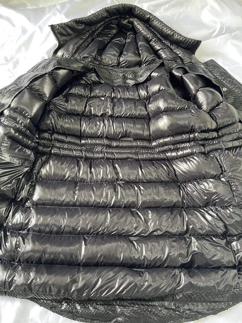 May include: A black, quilted puffer jacket with a hood. The jacket is made of a shiny, water-resistant material. The interior is also black and quilted. The jacket is designed for warmth and protection from the elements.