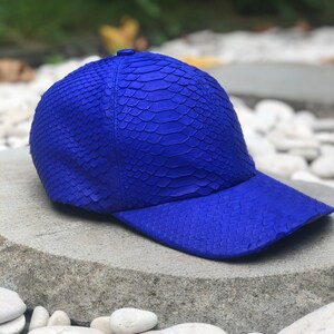 May include: A blue baseball cap made of snakeskin. The cap has a curved brim and a textured surface.