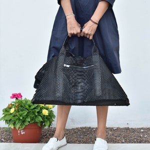 May include: A large black leather tote bag with a snakeskin pattern. The bag has a zipper closure and two top handles.
