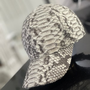 May include: A grey and white snakeskin baseball cap with a curved brim.