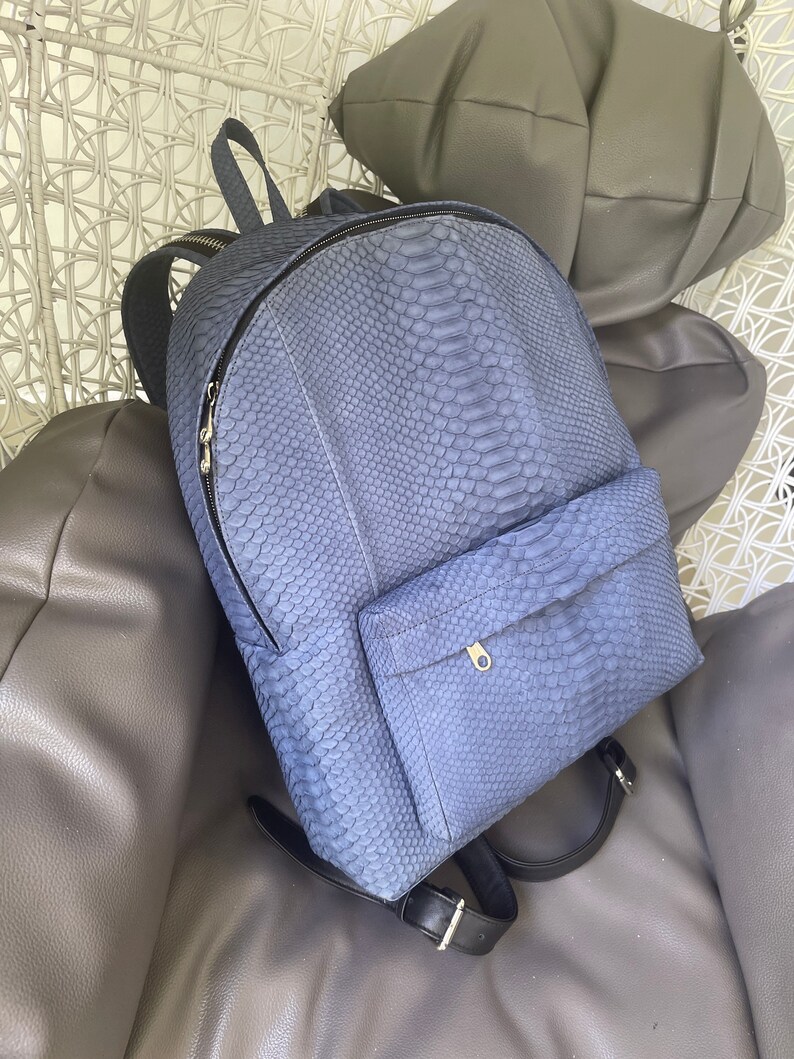 K&ouml;nnte beinhalten: Ein blauer Schlangenleder-Rucksack mit einer Rei&szlig;verschlusstasche vorne und verstellbaren Tr&auml;gern.