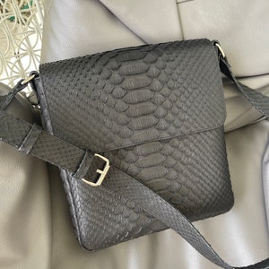 May include: A black leather messenger bag with a snakeskin pattern and a silver buckle.