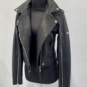 Może przedstawiać: Czarna sk&oacute;rzana kurtka ze wzorem sk&oacute;ry węża. Kurtka ma zamek błyskawiczny i st&oacute;jkę.