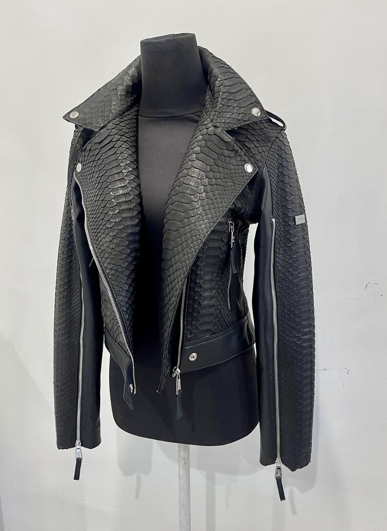 Może przedstawiać: Czarna sk&oacute;rzana kurtka ze wzorem sk&oacute;ry węża. Kurtka ma zamek błyskawiczny i st&oacute;jkę.